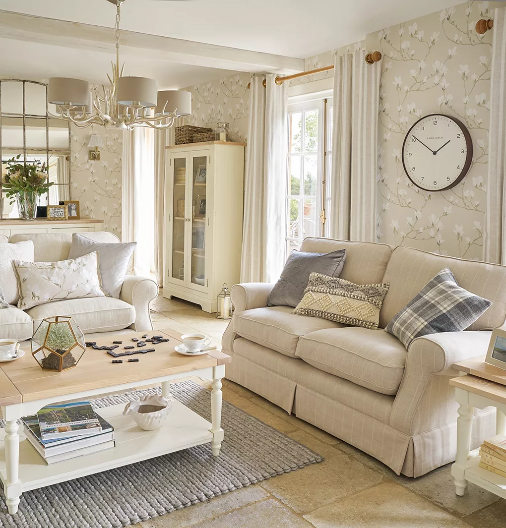 Giấy dán tường hình cây xanh trong phòng khách có ghế sofa màu xám đậm, đệm, thảm có họa tiết và bàn cà phê tròn bằng gỗ sáng màu.