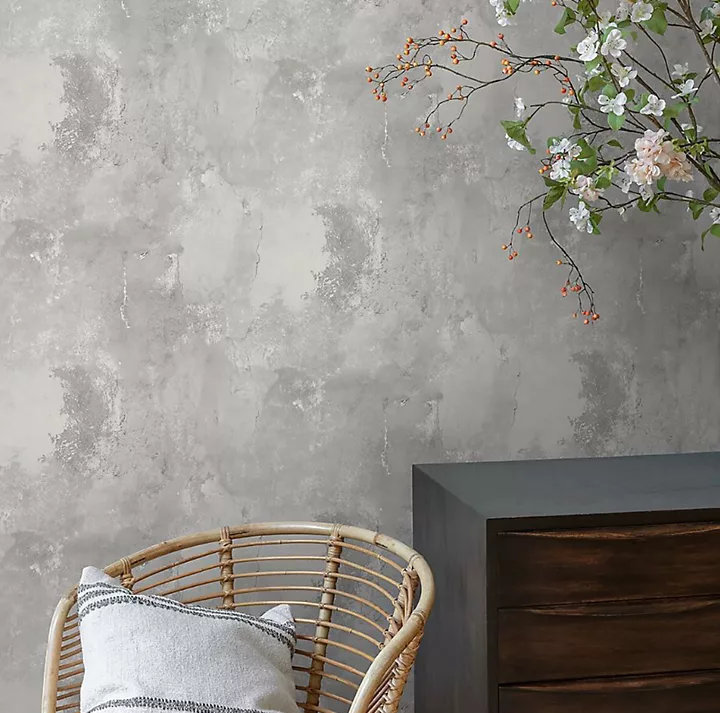 Phòng khách được trang trí bằng giấy dán tường hình cây xanh đậm, có ghế sofa góc lớn màu kem và bàn phụ bằng gỗ.