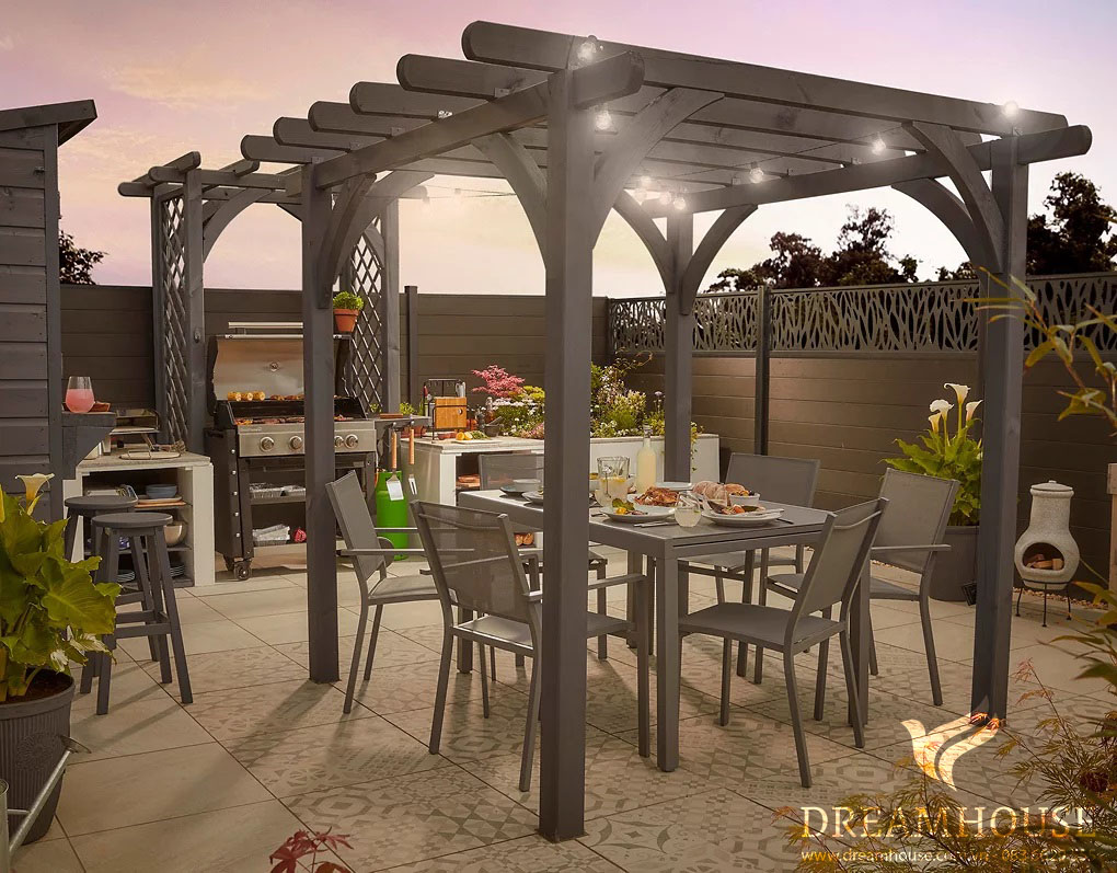 35-y-tuong-thiet-ke-canh-quan-san-vuon-cho-nam-2025-cho-nguoi-dam-me-25 Giàn che màu xám che phủ bộ bàn ăn ngoài vườn, phía sau là bếp ngoài trời.